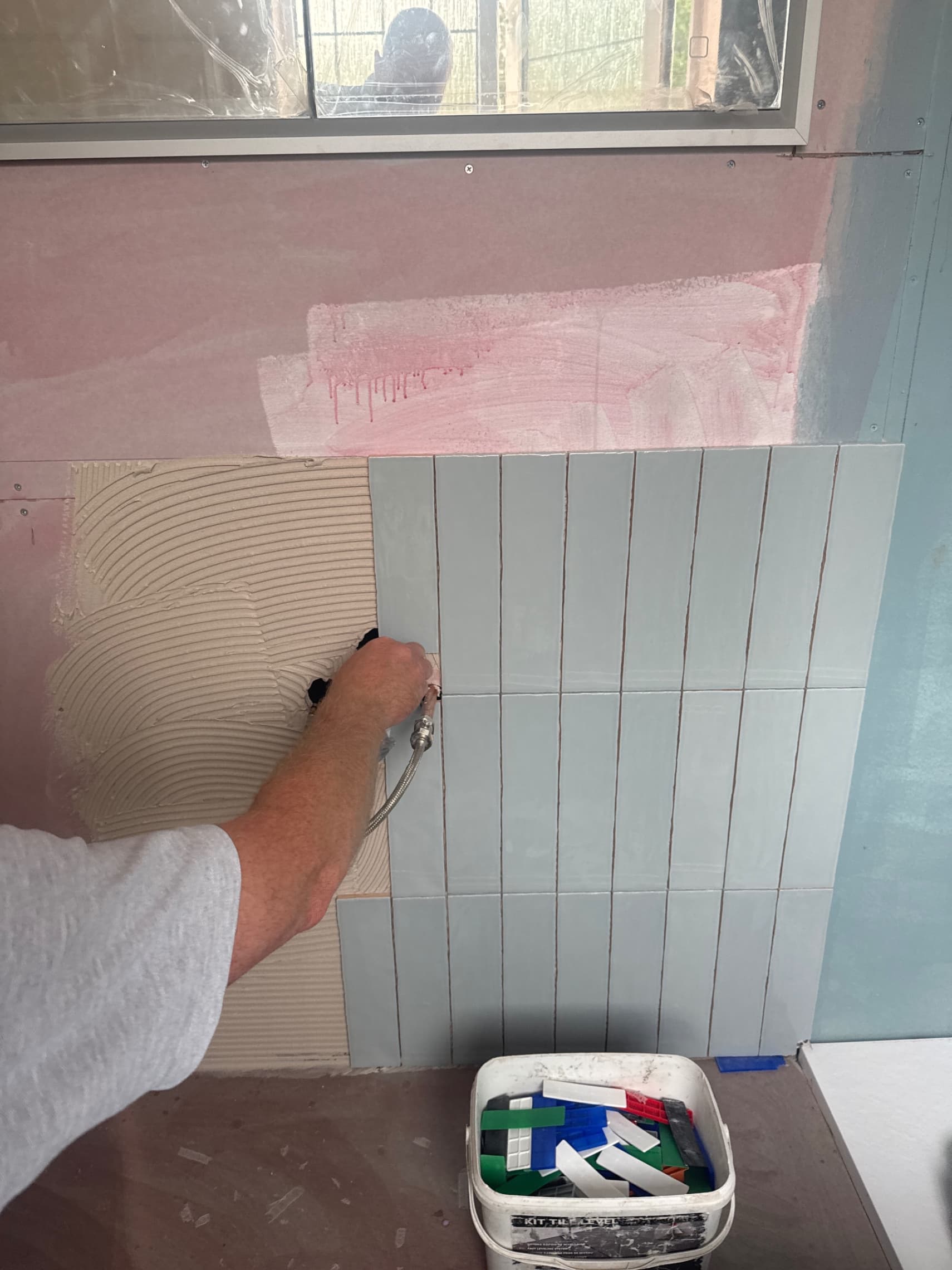 We've begun tiling this bathroom, applying a fresh vertical tile layout to the wall. Were using a notched trowel to ensure proper adhesive coverage before each tile is pressed into place.